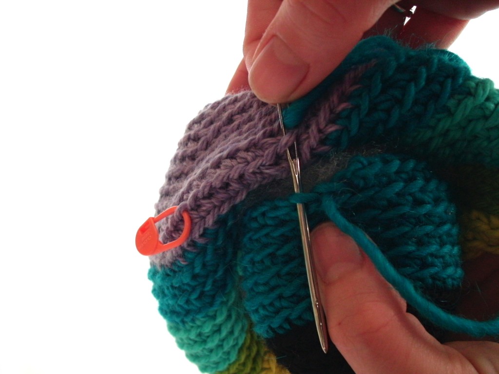 close up showing how to attach limbs to crochet stuffed animals - shows the tapestry needle going through one stitch on the leg and one stitch on the body