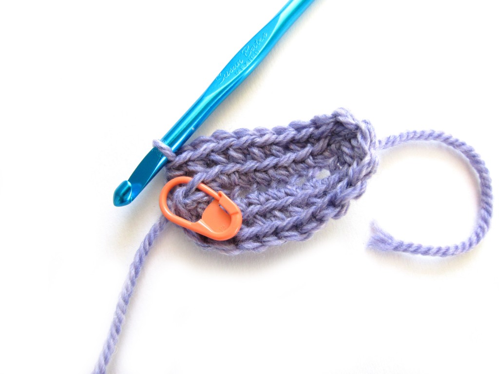 crocheted oval - lavender yarn - with blue hook and orange stitch marker still attached
